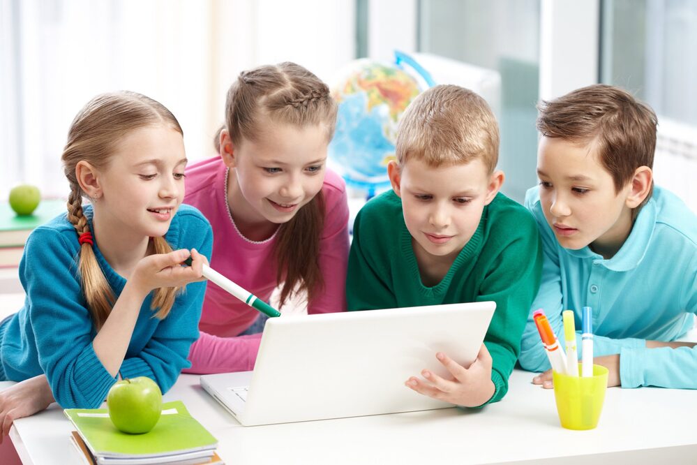 Children collaborating around a laptop in a bright classroom setting.